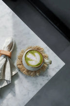 Tasse en céramique crème avec latte matcha vert clair et mousse blanche sur sous-verre texturé