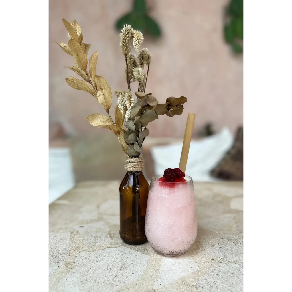 Boisson rose avec topping rouge et paille en bambou, bouteille avec feuilles séchées