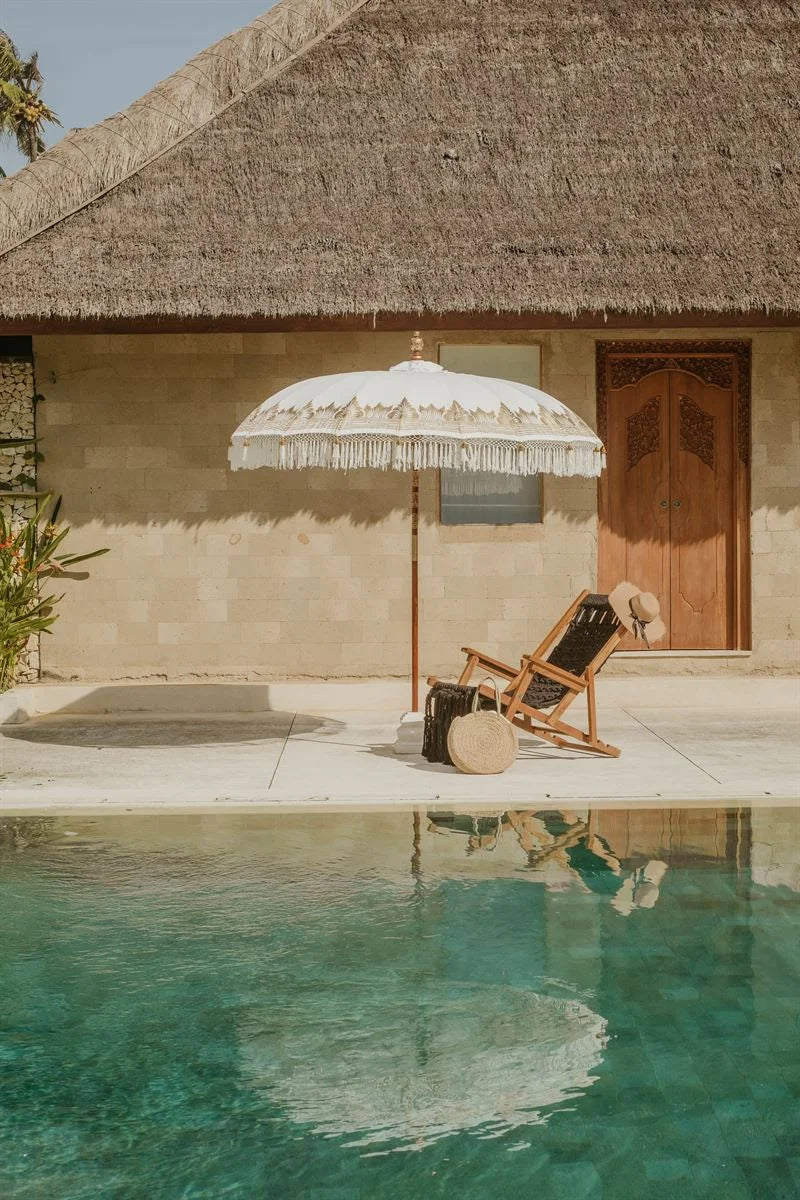 Ambiance détendue avec parasol rond crème à franges et bordures dorées pour extérieur