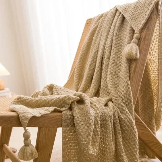 Couverture tricotée beige bohème avec pompons sur une chaise en bois