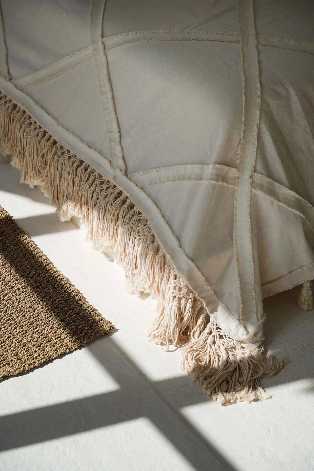 Plaid en coton écru avec franges longues et pompons décoratifs sur un lit