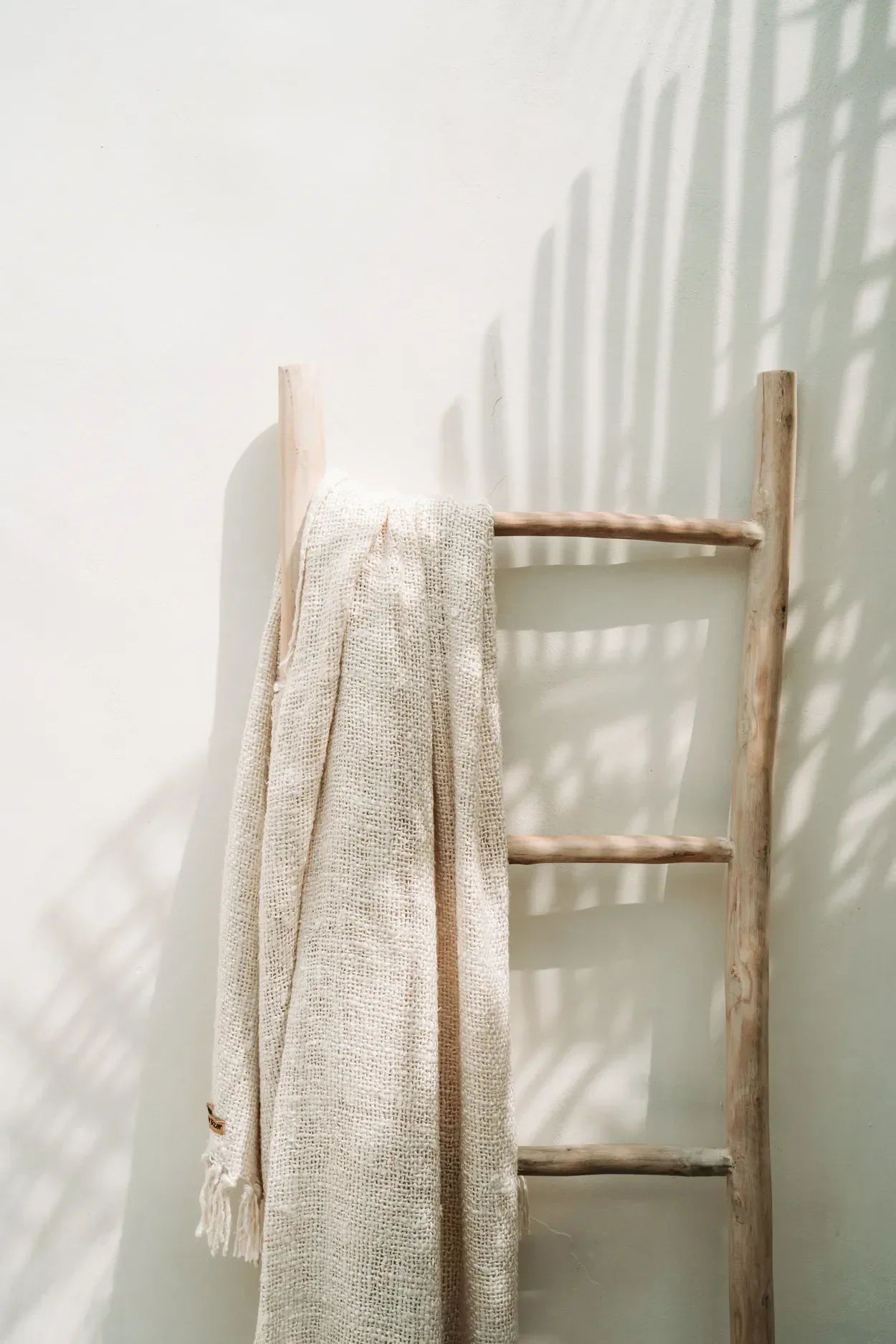Plaid en coton gaufré crème avec franges décoratives, drapé sur une échelle en bois