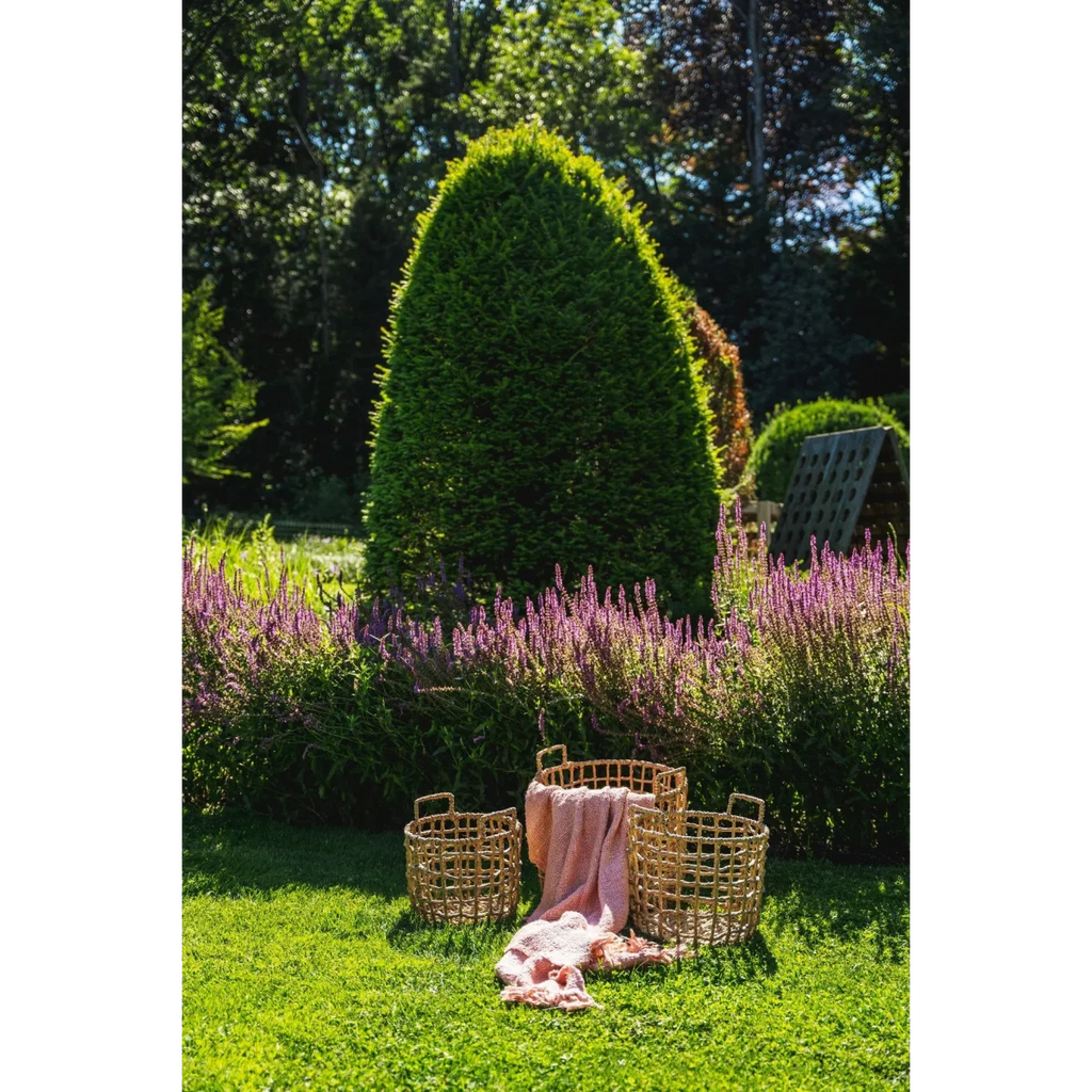 Trois paniers en rotin avec une couverture rose saumon dans un jardin coloré