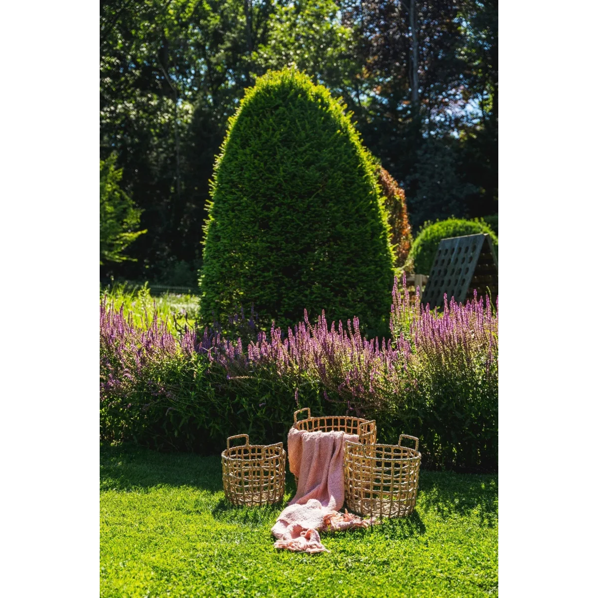 Trois paniers en rotin avec une couverture rose saumon dans un jardin coloré