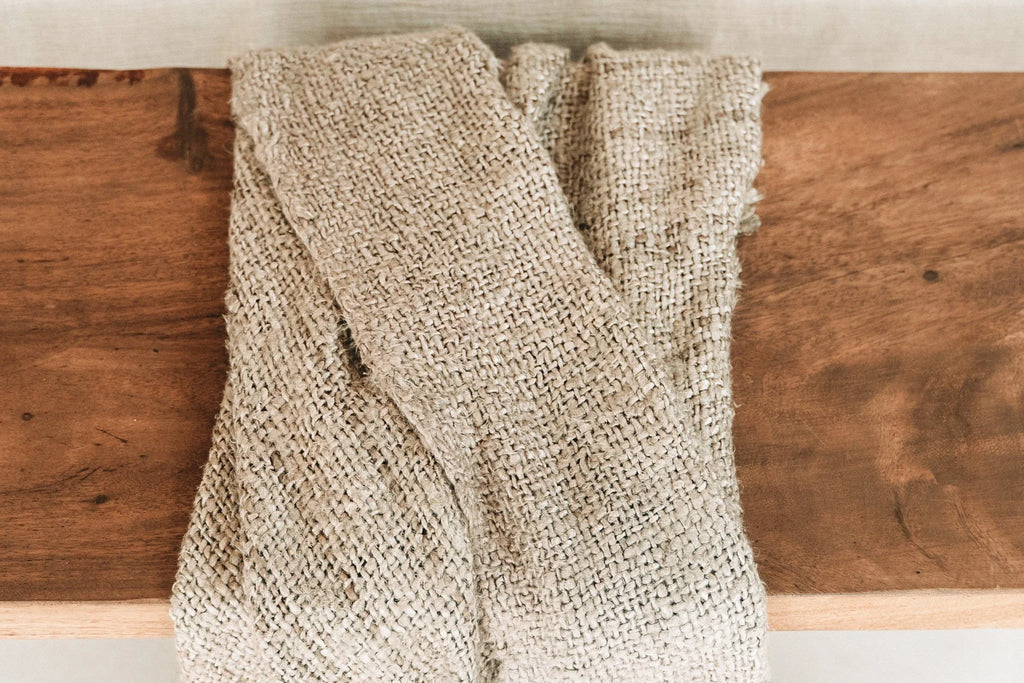 Tissu tissé beige à franges, plié sur une surface en bois, pour décoration lit ou canapé