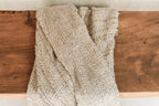 Tissu tissé beige à franges, plié sur une surface en bois, pour décoration lit ou canapé