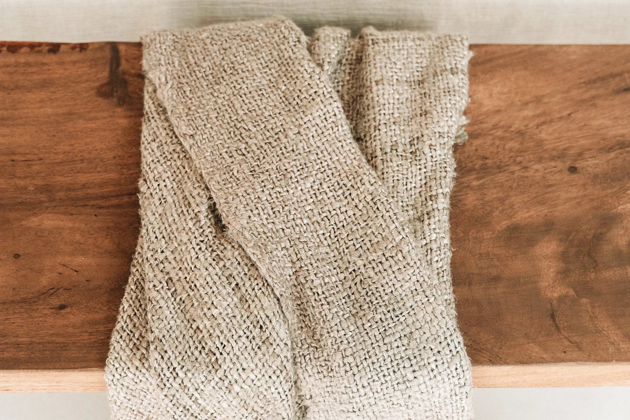Tissu tissé beige à franges, plié sur une surface en bois, pour décoration lit ou canapé