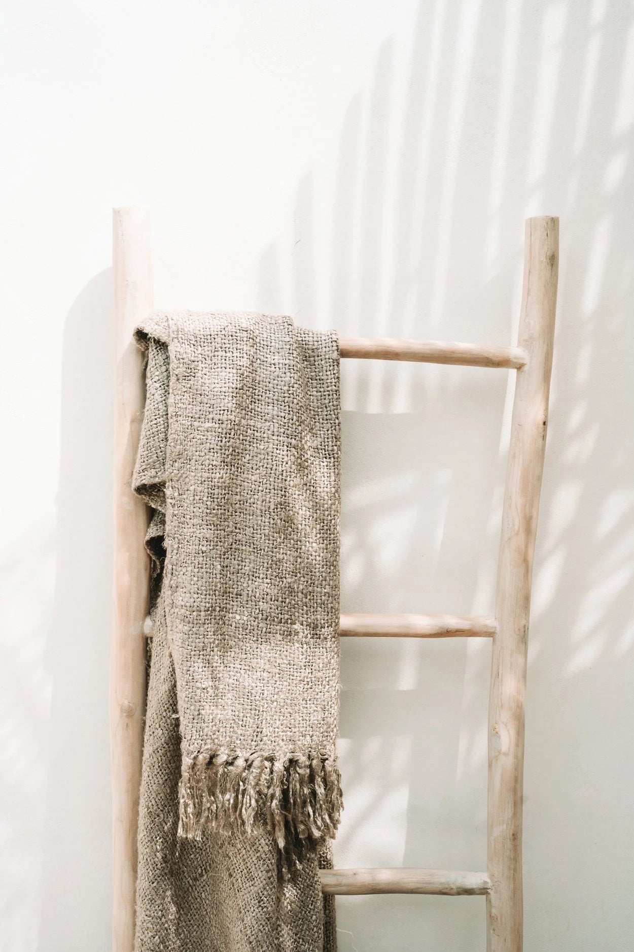 Plaid en coton tissé beige avec franges, drapé sur une échelle en bois clair