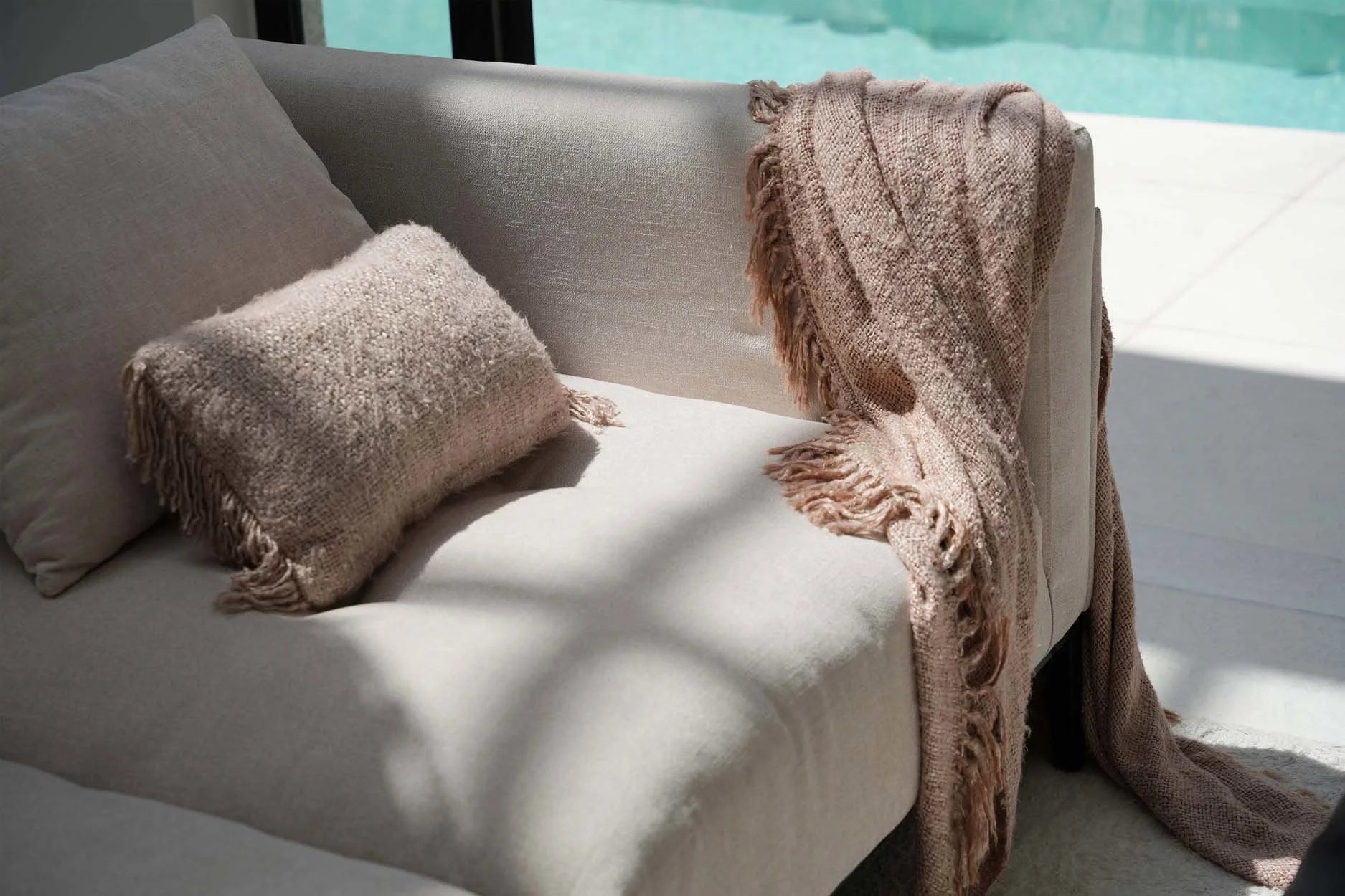 Canapé beige avec coussins texturés et plaid à franges pour décoration intérieure