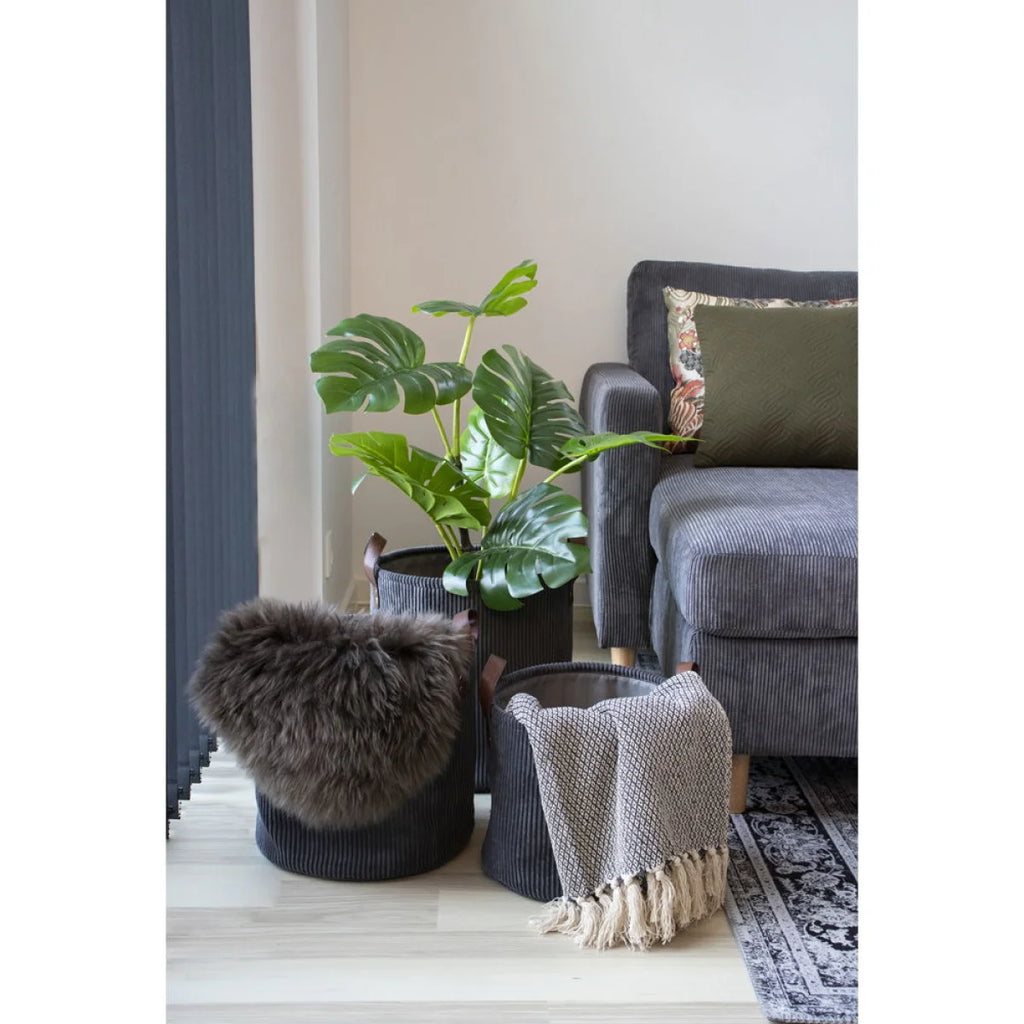 Panier de rangement en tissu côtelé gris foncé avec poignées en bois, couverture en laine brune et plante monstera
