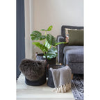 Panier de rangement en tissu côtelé gris foncé avec poignées en bois, couverture en laine brune et plante monstera