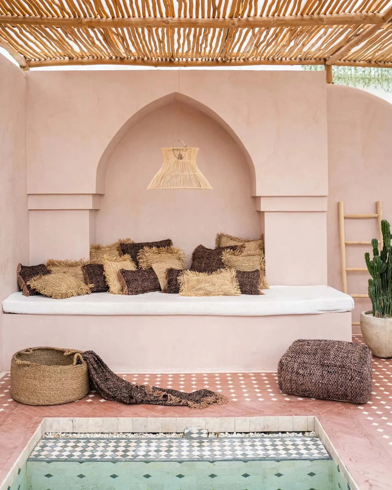 Coin salon extérieur marocain avec banquette, coussins et petite piscine, plaid en coton noir cuivre