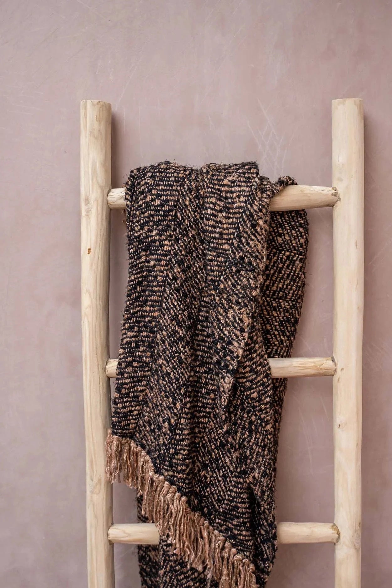Plaid en coton tissé noir cuivre à franges chevrons sur une échelle en bois