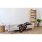 Canapé-jour beige capitonné, pieds bois, plaid duveteux marron foncé frangé