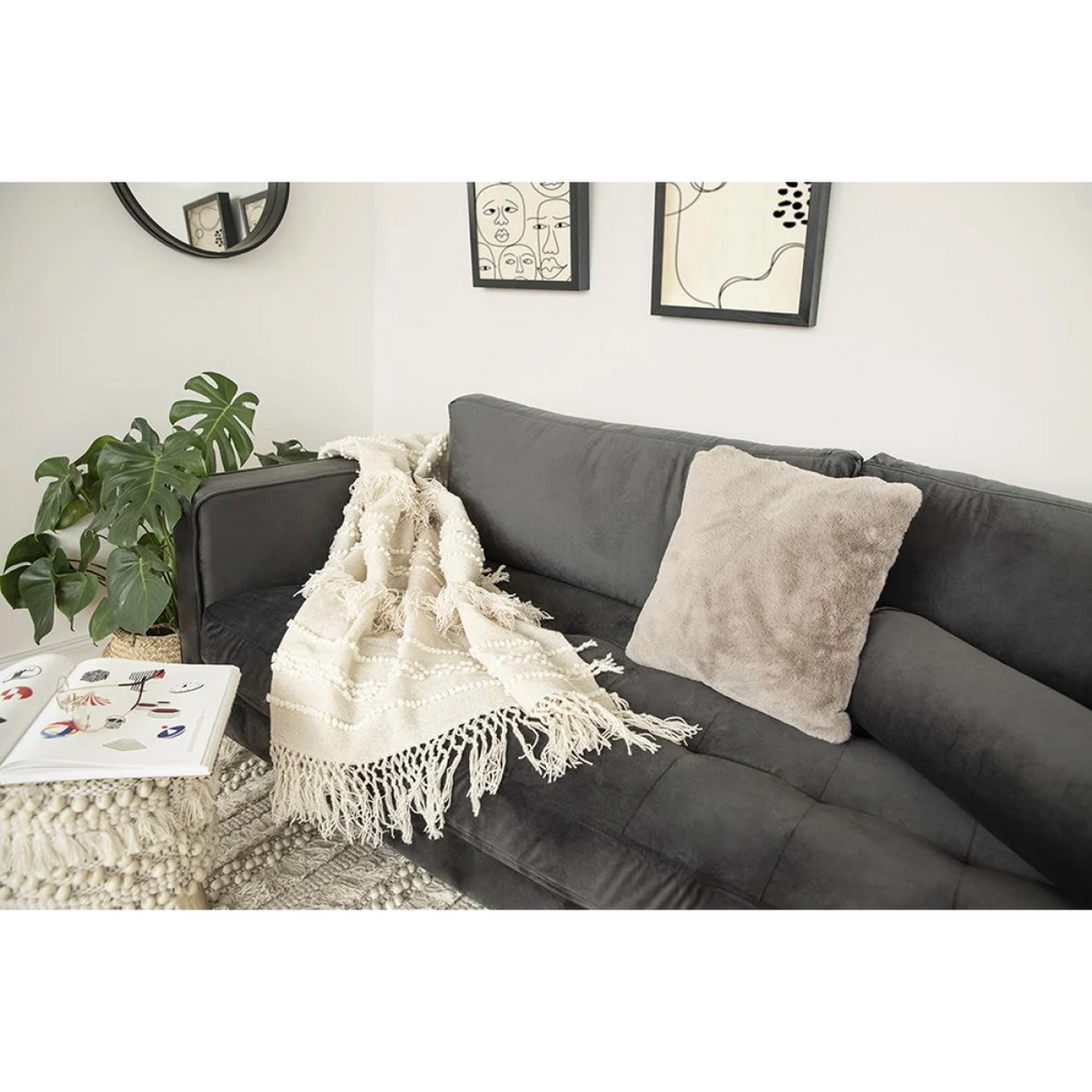 Canapé en velours gris foncé avec plaid en laine écrue à franges et motifs en relief