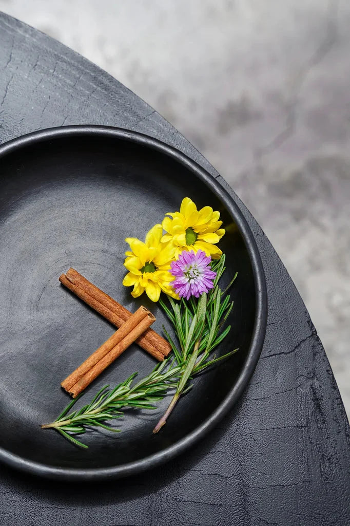 Assiette noire avec bâtons de cannelle, romarin et fleurs.