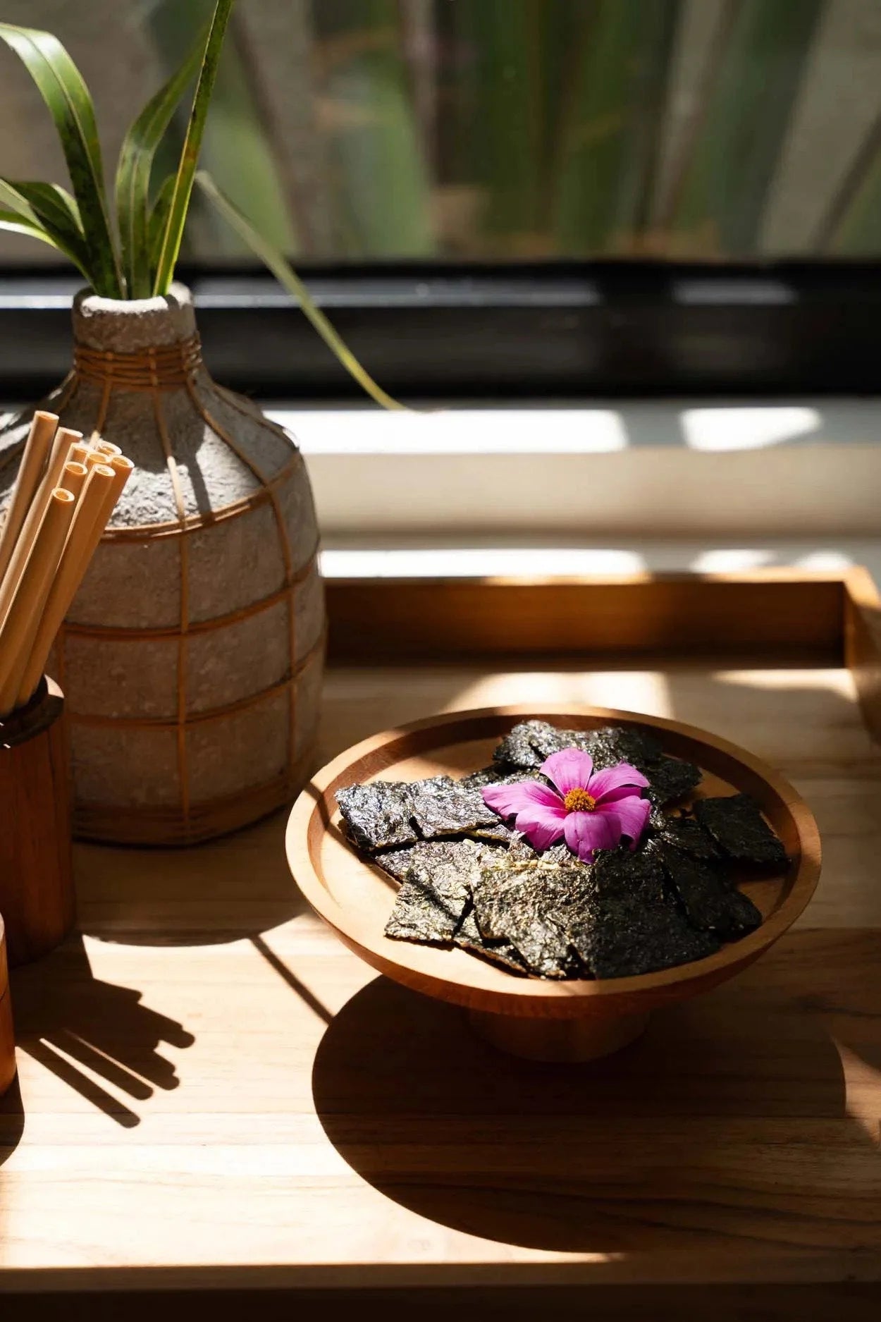 Crispy seaweed snacks garnis d’une fleur rose sur un plat en teck naturel en bois massif