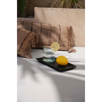 Verre d’eau avec tranche de citron et citron entier sur plateau en terre cuite noire mat