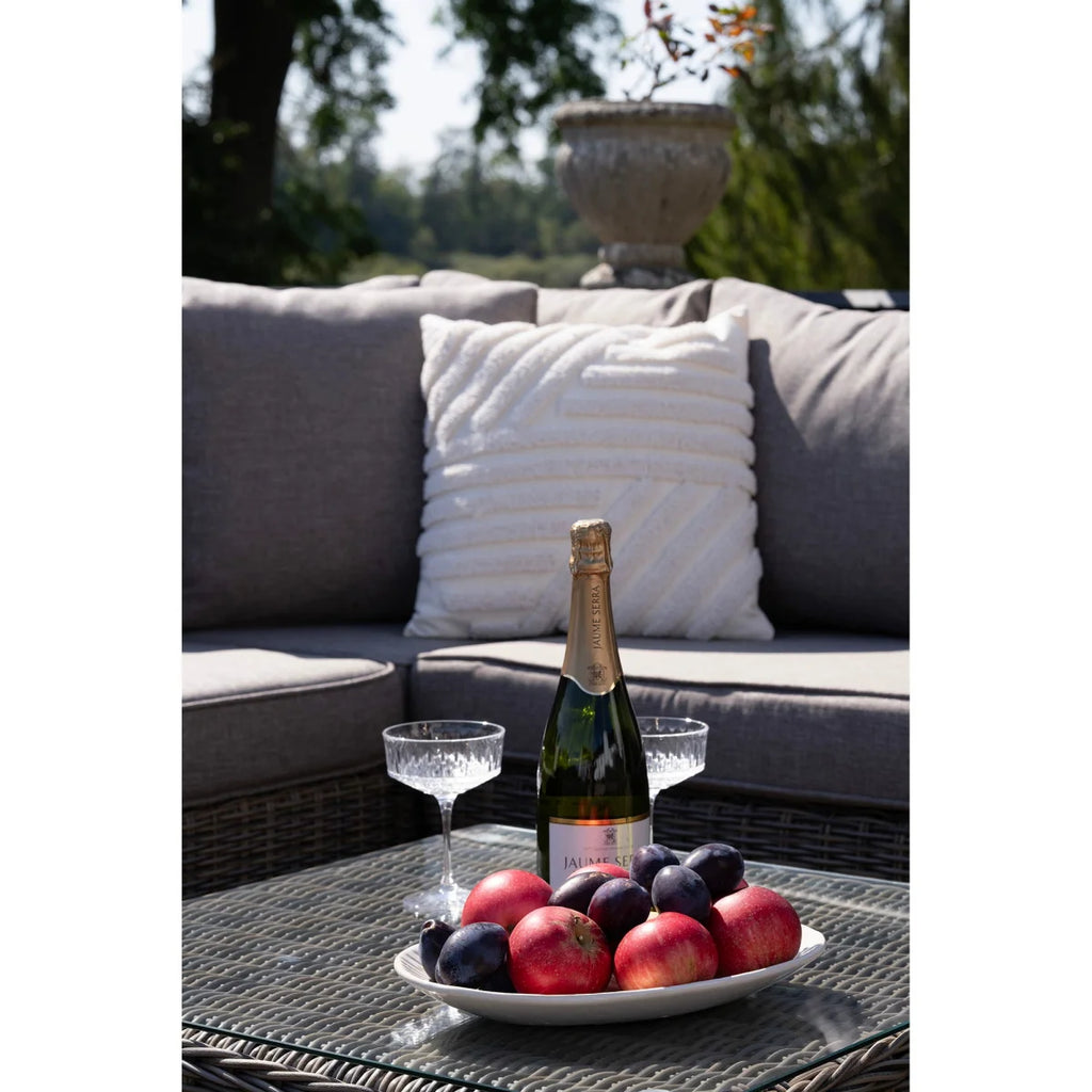 Bouteille de vin pétillant Jules & Cie verte en verre, avec liège en foil doré et étiquette, près de deux flûtes à champagne en cristal sur une table extérieure