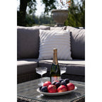 Bouteille de vin pétillant Jules & Cie verte en verre, avec liège en foil doré et étiquette, près de deux flûtes à champagne en cristal sur une table extérieure