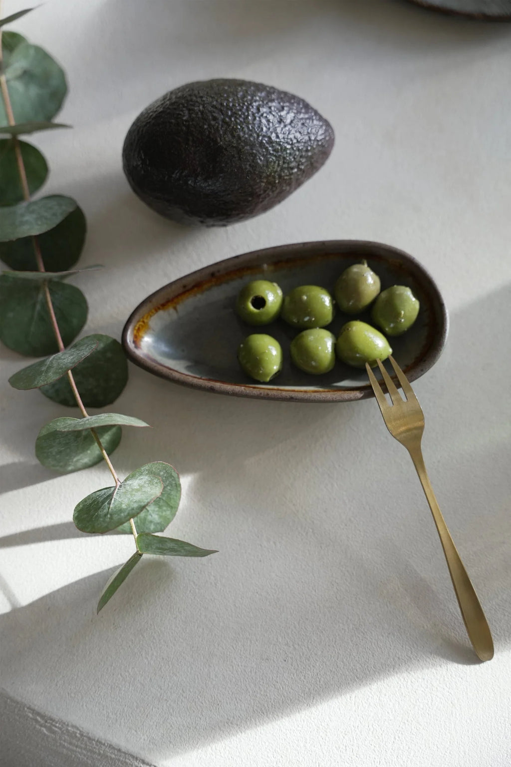 Bol en céramique texturée sombre avec olives vertes et fourchette dorée
