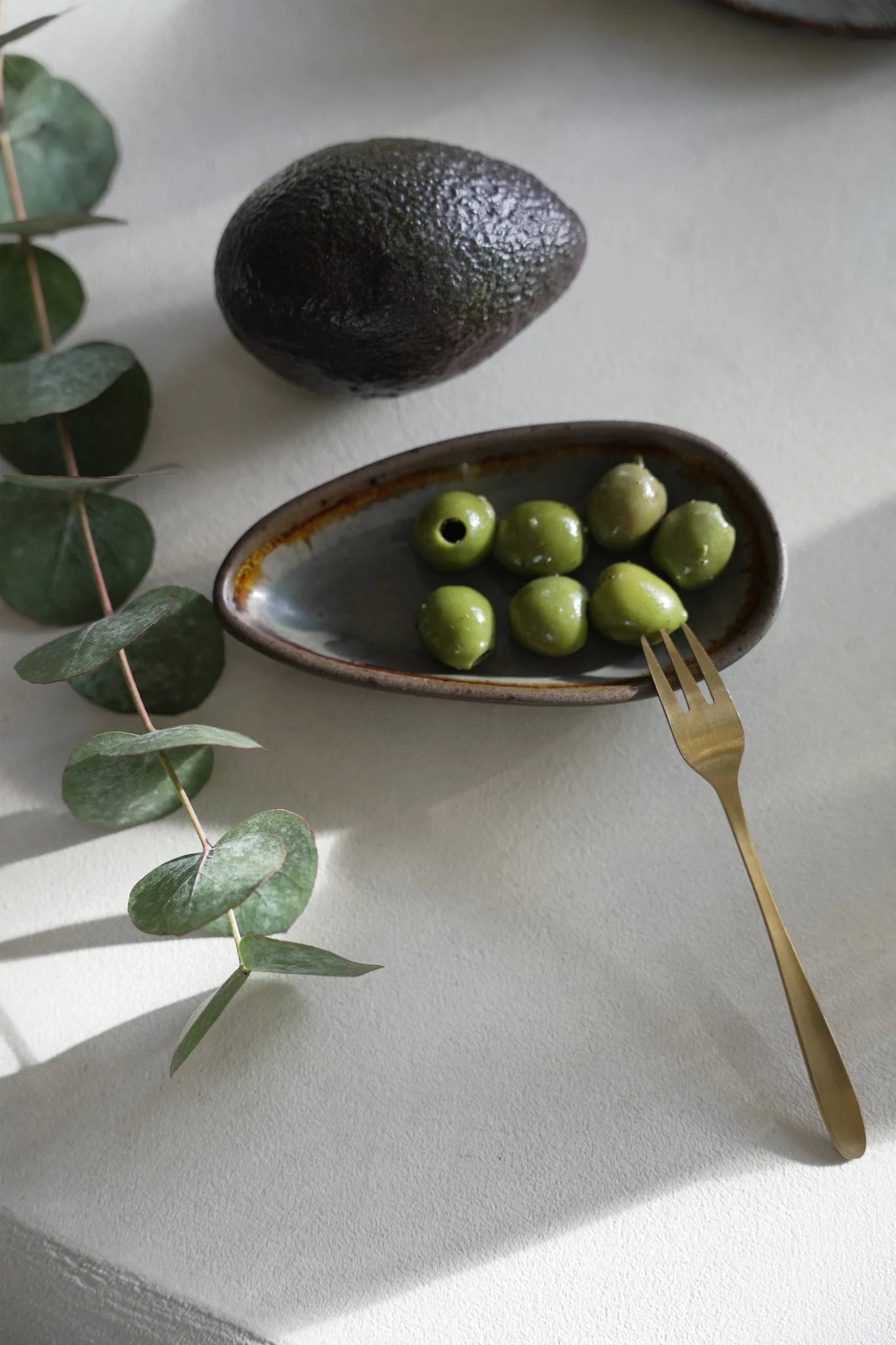 Bol en céramique texturée sombre avec olives vertes et fourchette dorée