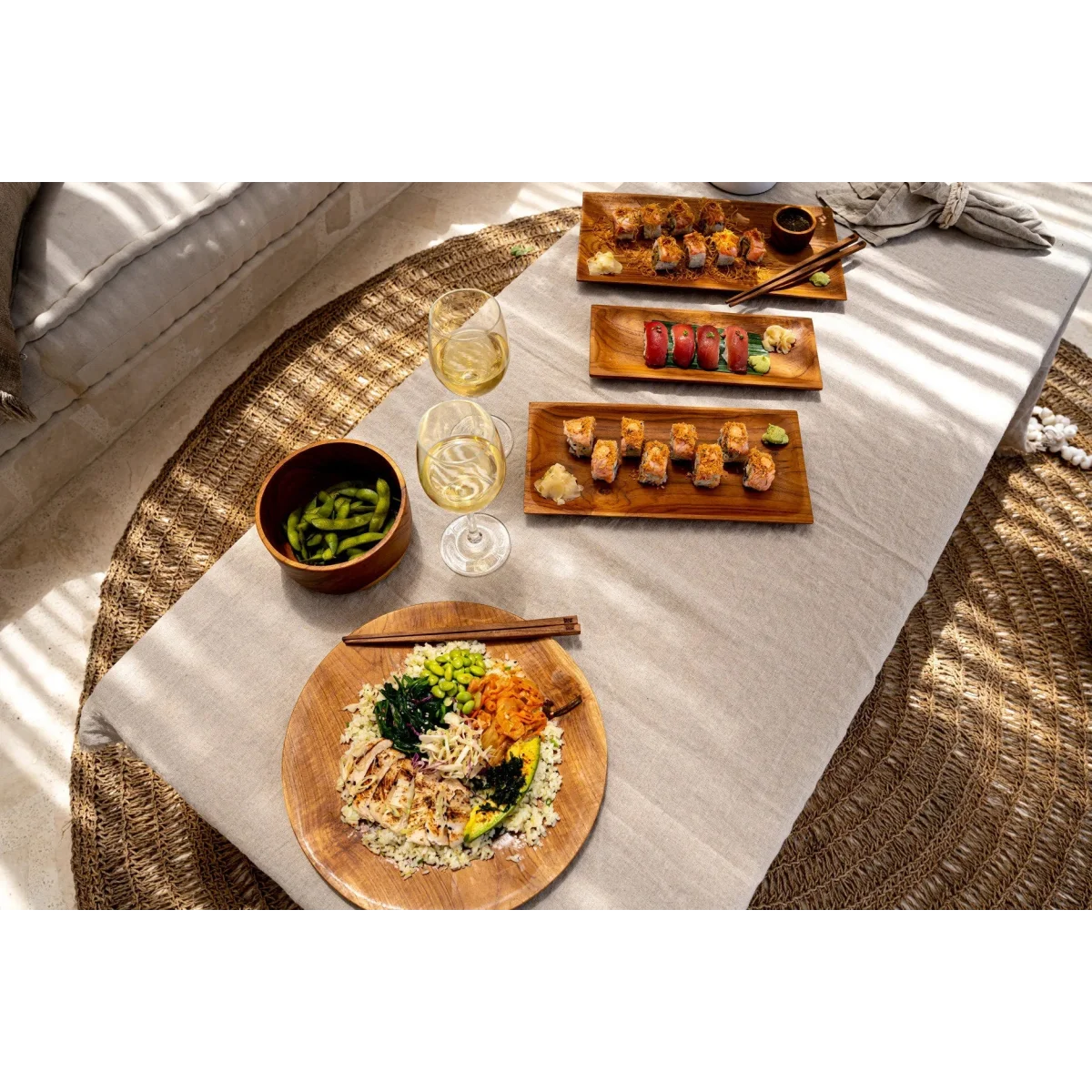Assortiment de sushi, edamame et poke bowl avec vin sur plateau rectangulaire en teck