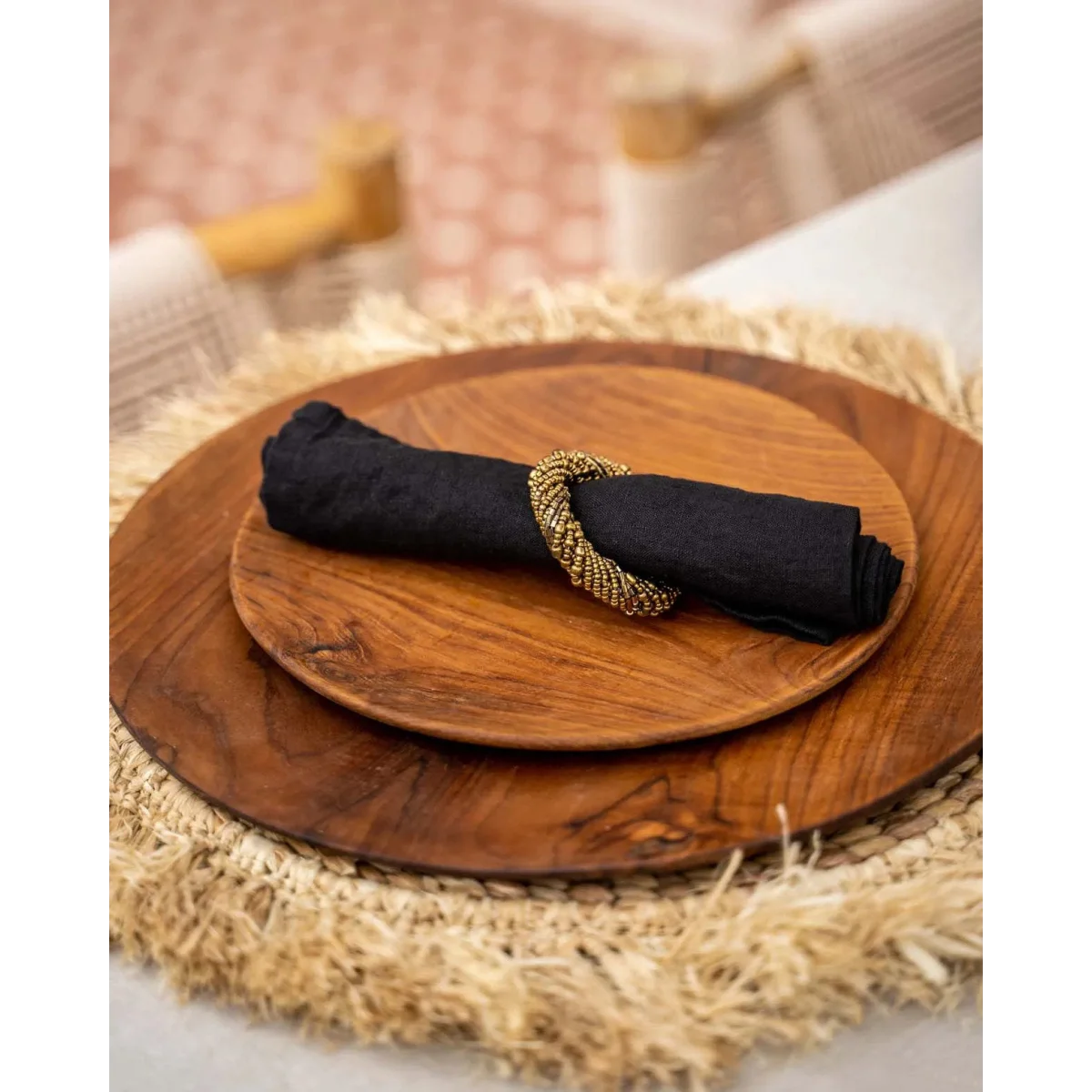 Serviette en lin noire avec anneau en perles dorées sur deux assiettes en bois rondes