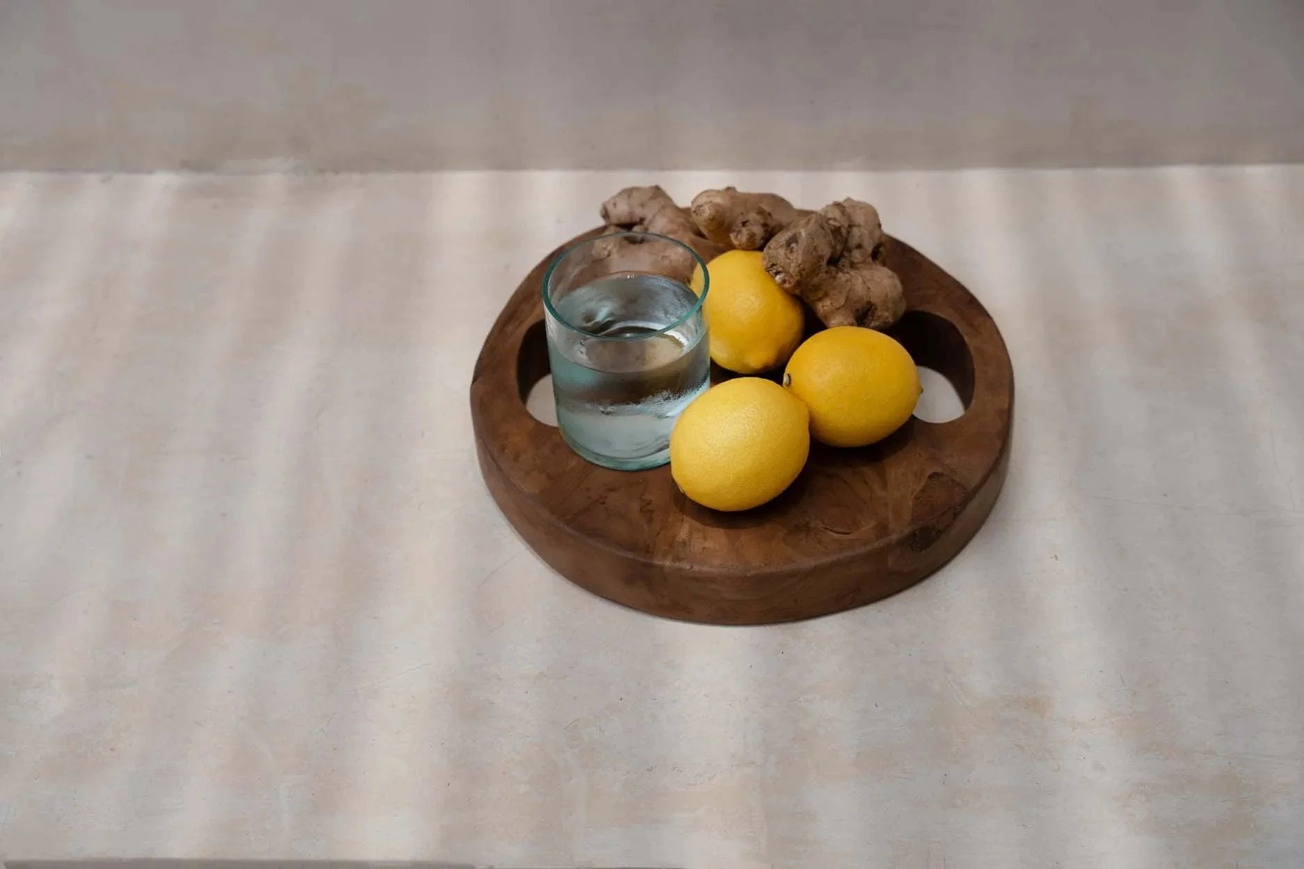 Plateau rond en teck naturel avec poignées ajourées, contenant citrons, gingembre et eau