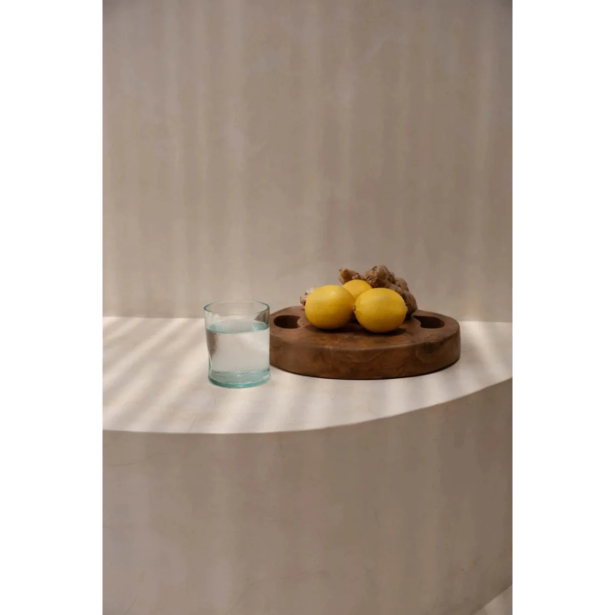 Plateau rond en teck naturel avec poignées ajourées, contenant trois citrons et gingembre