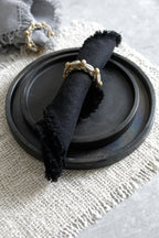 Serviette frangée noire avec anneau en perles sur une assiette en terre cuite noire
