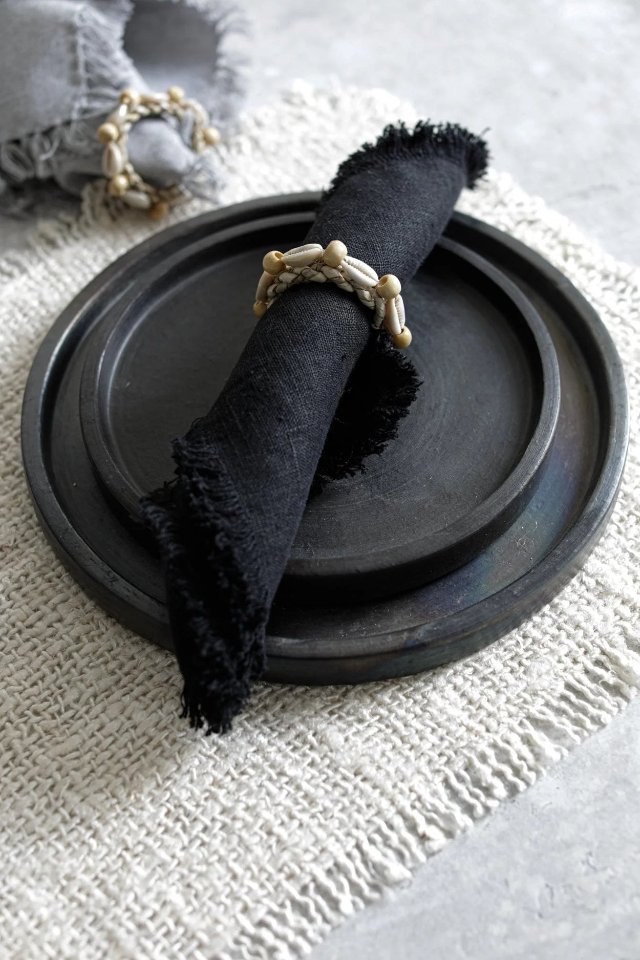 Serviette frangée noire avec anneau en perles sur une assiette en terre cuite noire