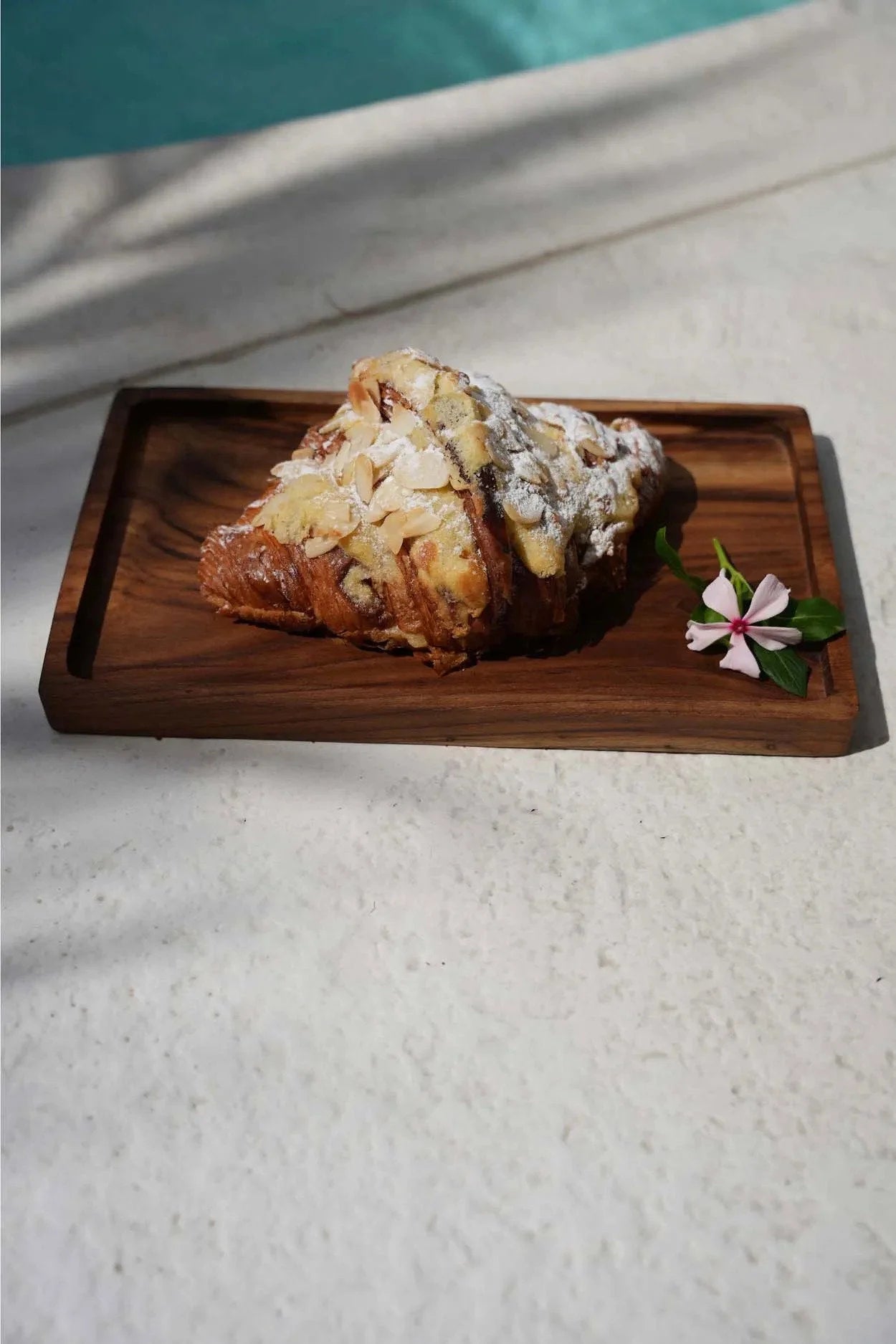 Croissant aux amandes saupoudré de sucre glace sur plateau en teck rectangulaire naturel