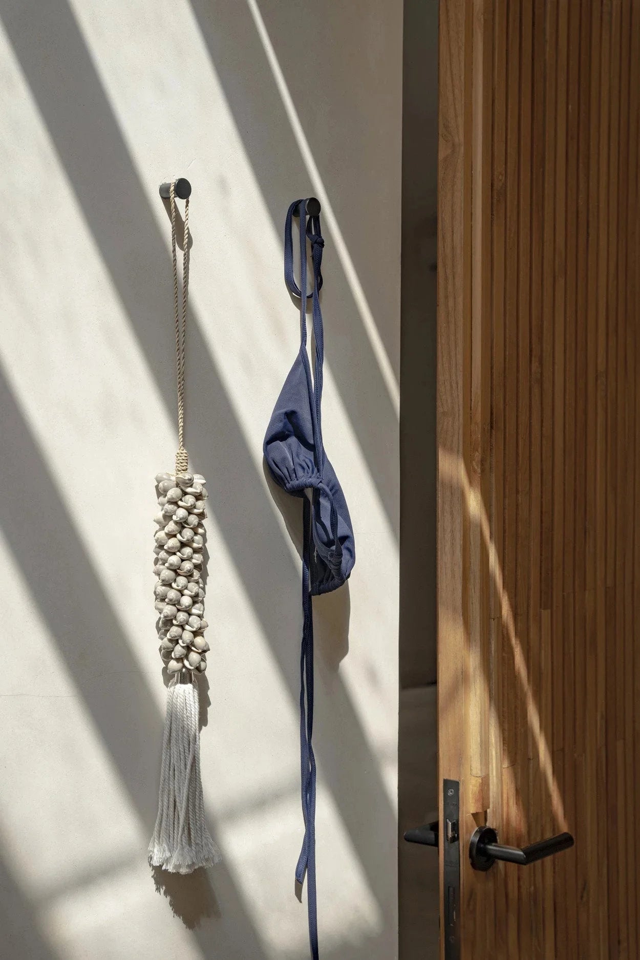 Bikini bleu suspendu sur un mur dans le mural Pompon en coquillages et coton gris perle