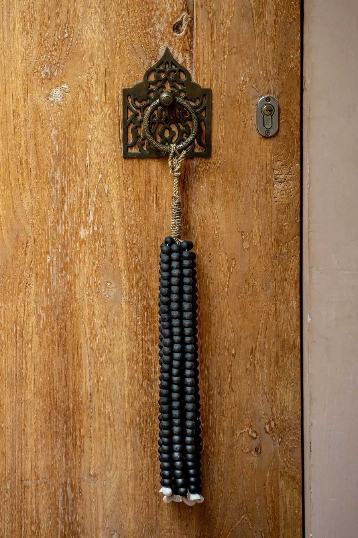Poignée de porte ornée avec pampille de perles de bois noires suspendue par un cordon naturel
