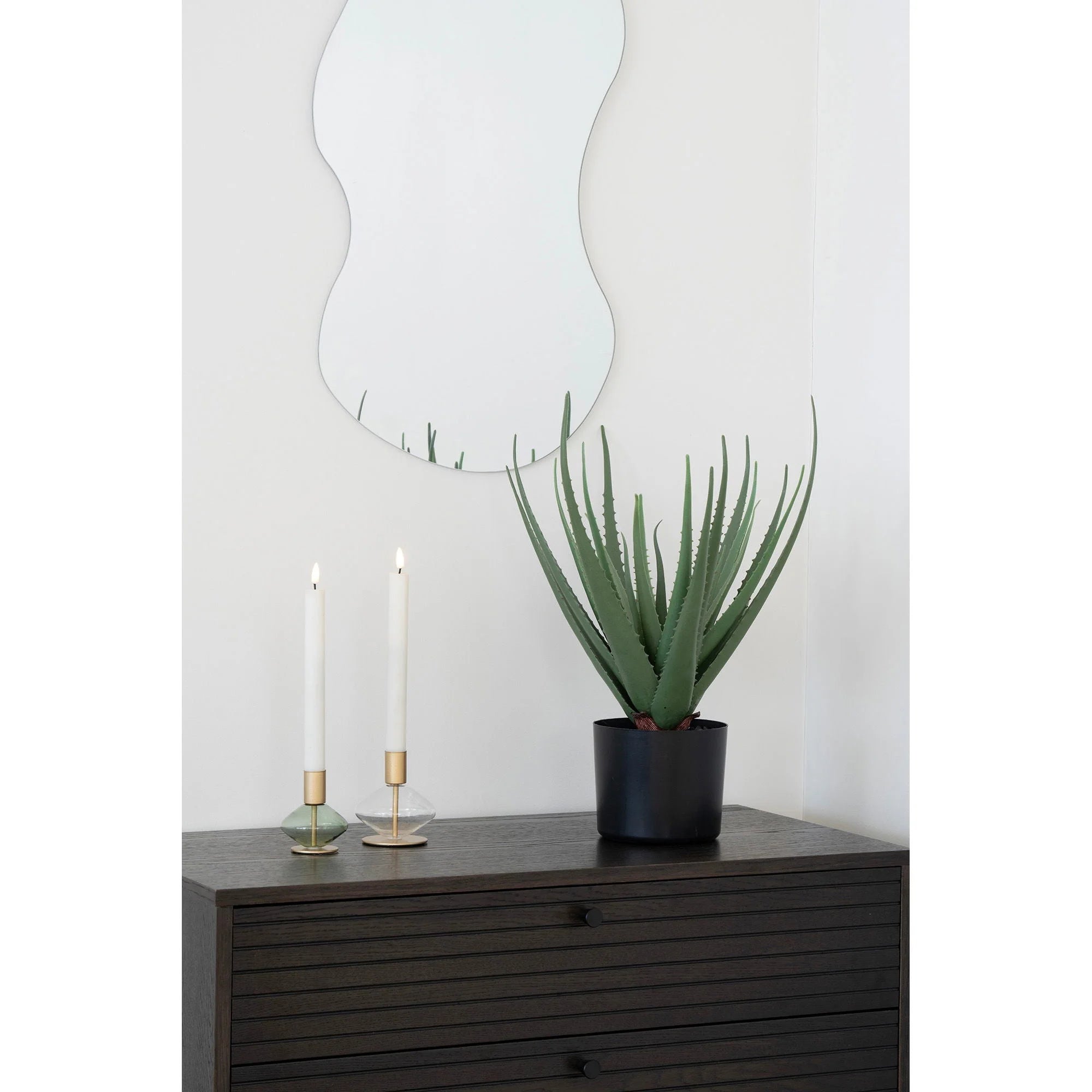 Décor intérieur avec miroir, plante et bougies dans porte-bougie en verre et métal doré vert