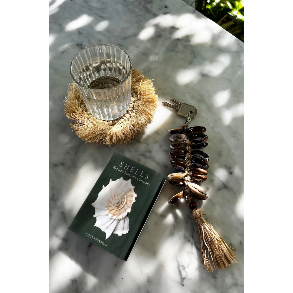 Livre vert foncé avec coquillage blanc sur la couverture, porte-clés en coquillages et raphia