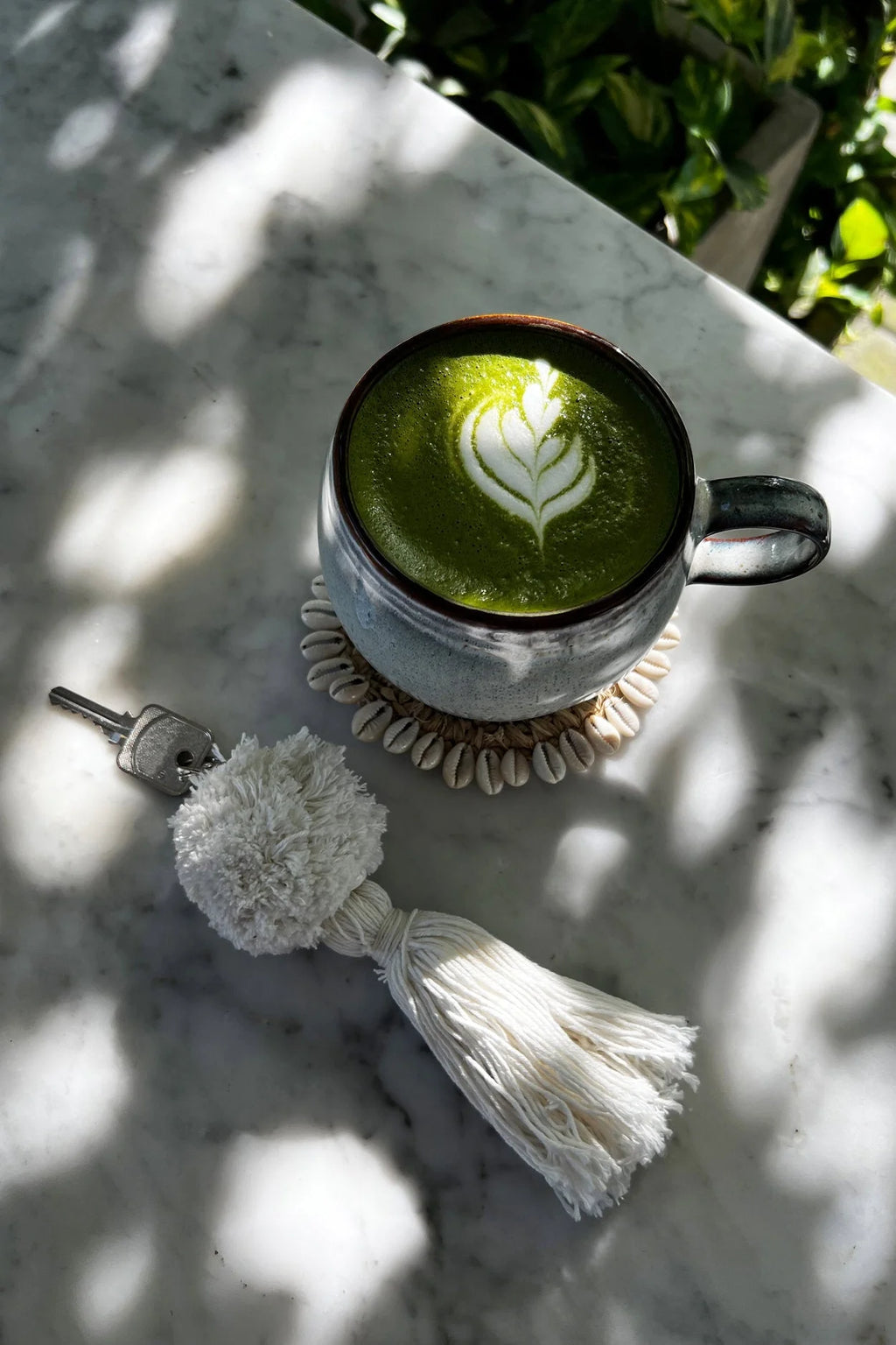 Tasse en céramique avec latte matcha vert foncé et mousse feuille blanche sur sous-verre coquillages tressé