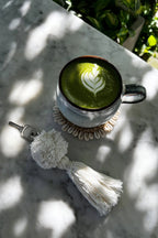 Tasse en céramique avec latte matcha vert foncé et mousse feuille blanche sur sous-verre coquillages tressé