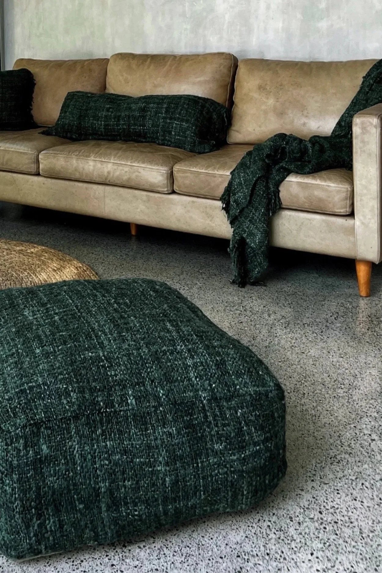 Canapé en cuir beige avec coussins verts foncés et plaid dans le salon