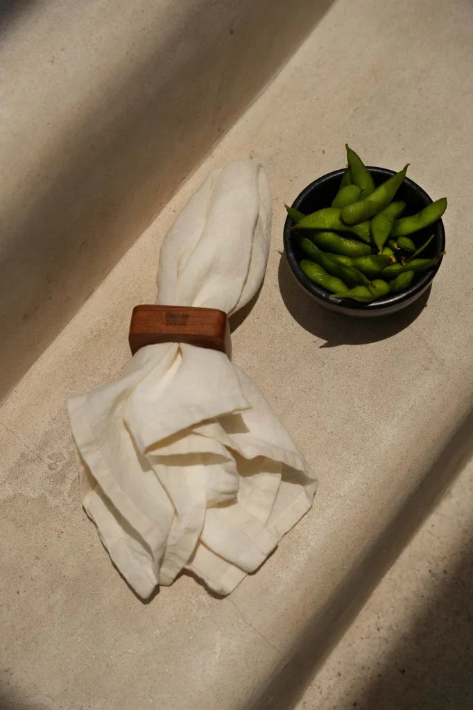 Edamame dans un bol foncé à côté d’une serviette en lin blanc avec un rond de serviette marron.