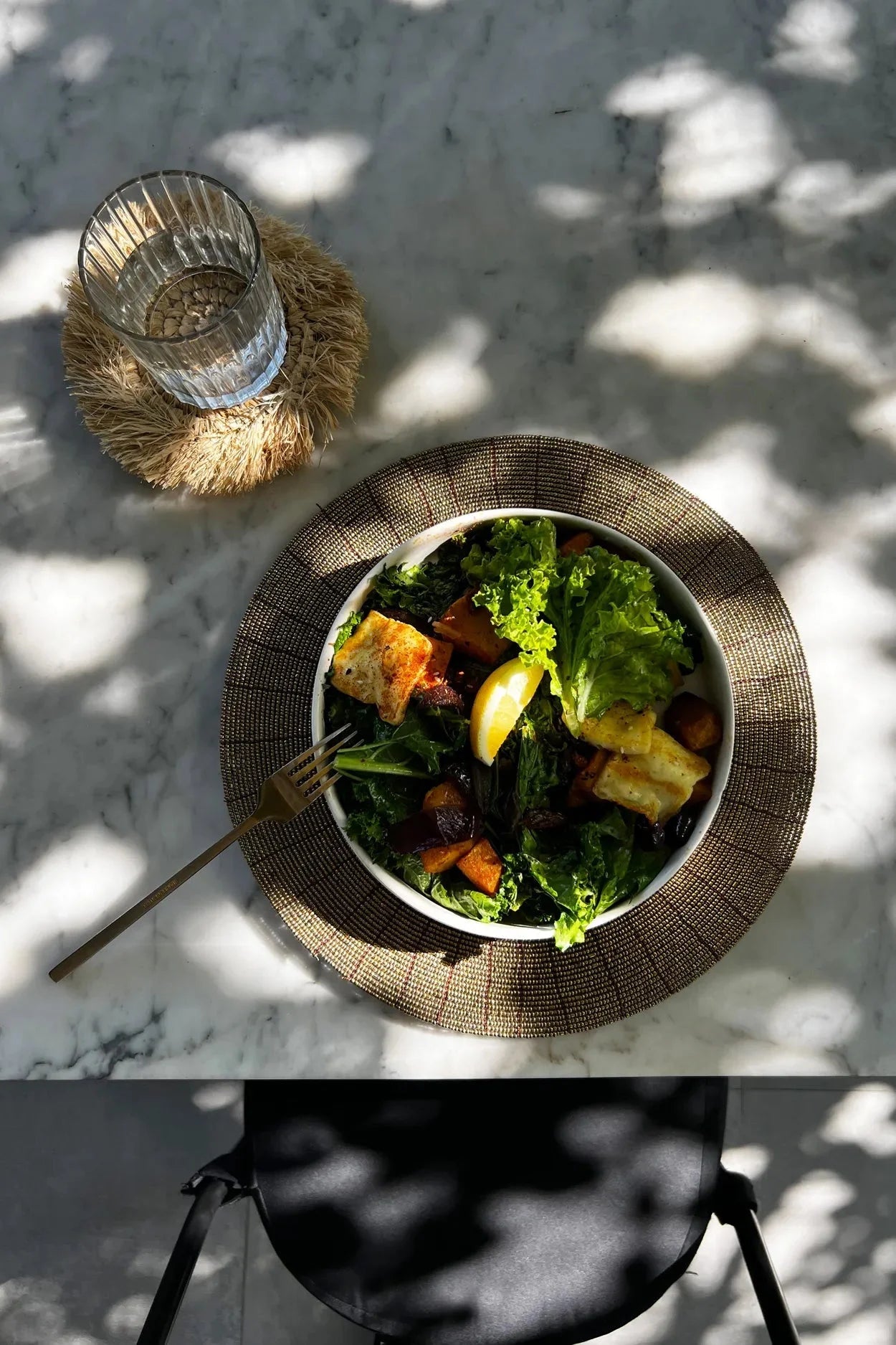Salade colorée avec légumes rôtis, greens, et tranche de citron sur un set de table rond doré