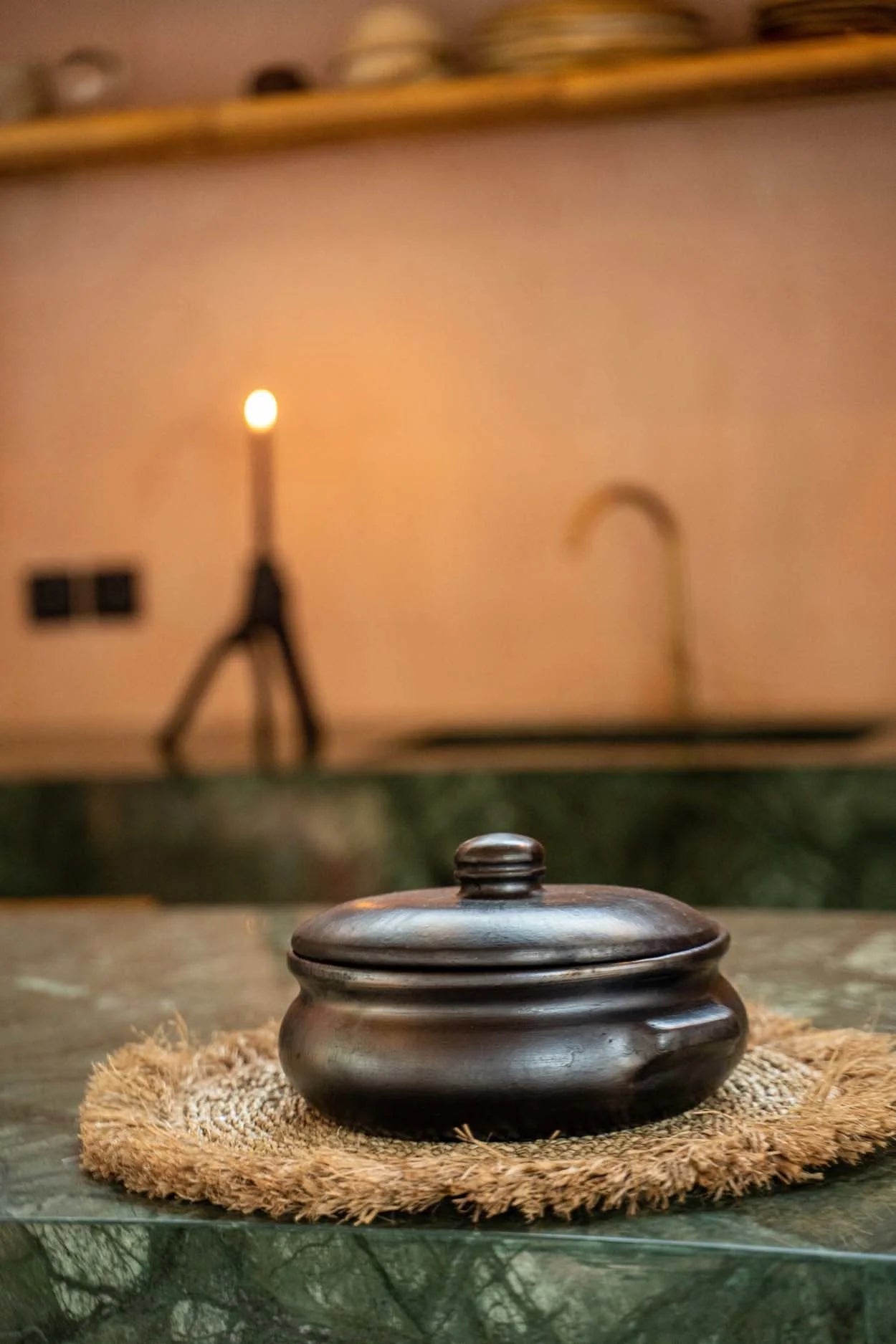 Pot en terre cuite noire avec couvercle sur un tapis tissé, parfait pour la table