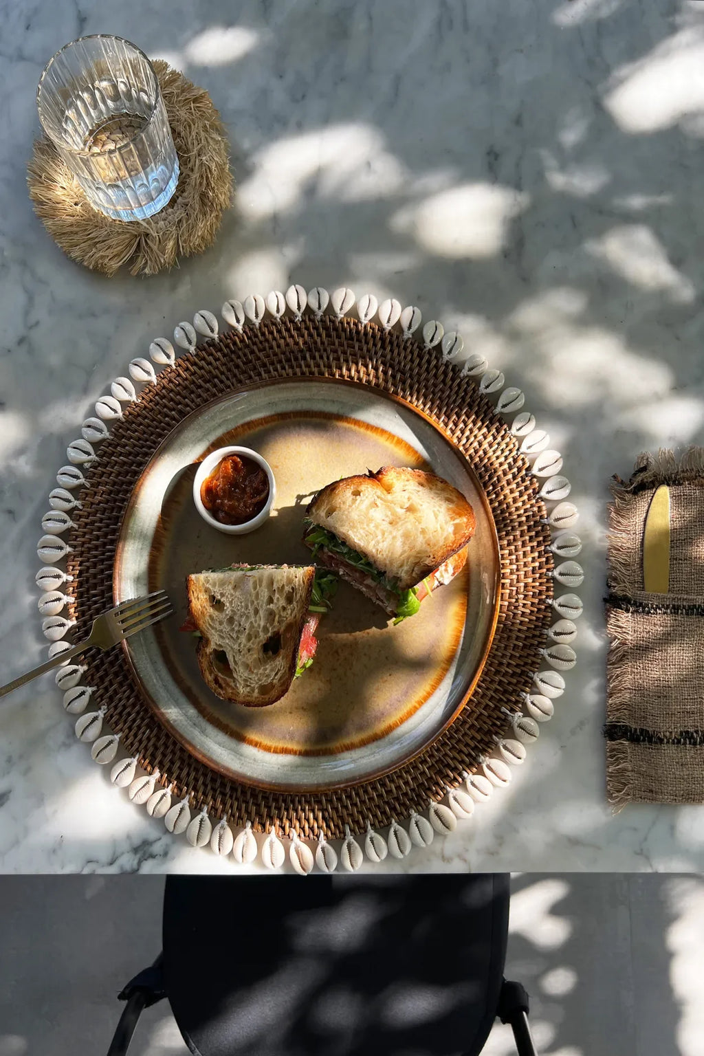 Sandwich présenté sur une assiette rotin marron avec bordure de coquillages cauris