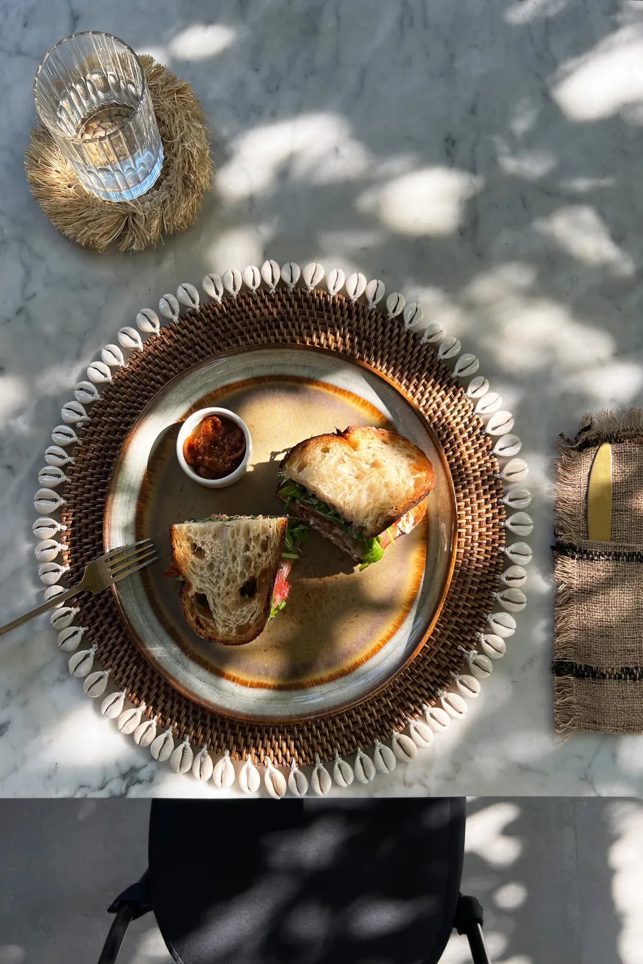 Sandwich présenté sur une assiette rotin marron avec bordure de coquillages cauris