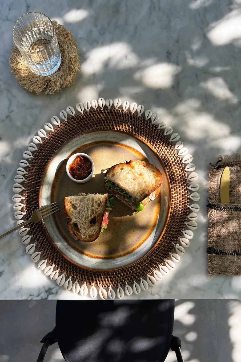Sandwich avec sauce sur un set de table rond en rotin marron avec bordure de coquillages cauris