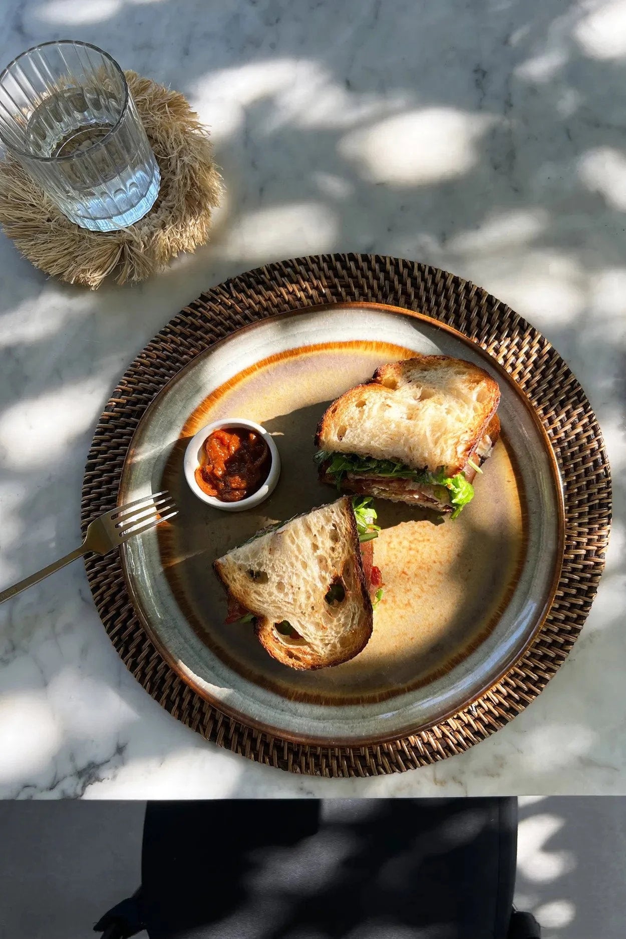 Sandwich sur une assiette avec sauce, set de table rond en rotin tressé marron naturel
