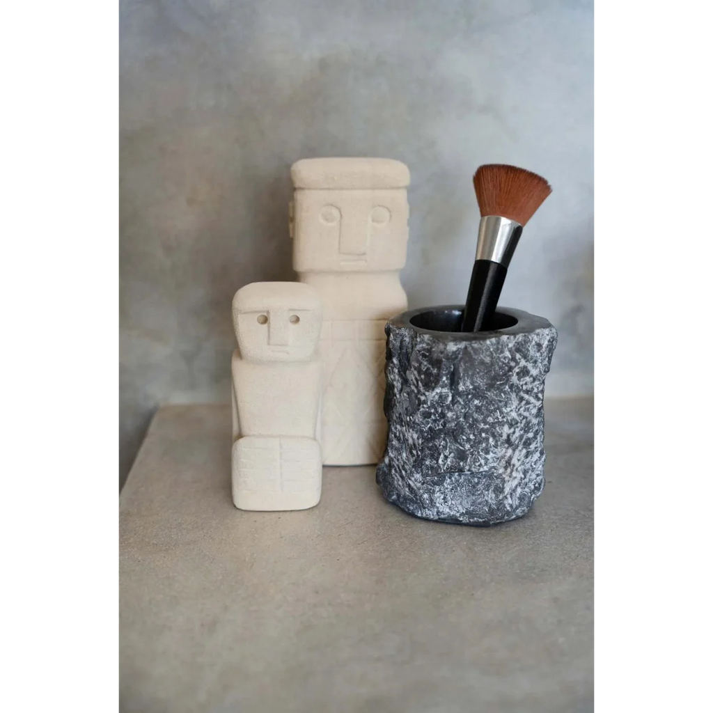 Pinceau de maquillage dans un porte-pierre texturé à côté de sculptures minimalistes