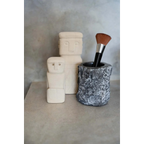 Pinceau de maquillage dans un porte-pierre texturé à côté de sculptures minimalistes