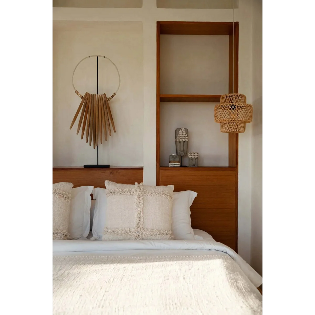 Décor de chambre avec lit blanc, coussins décoratifs, accents en bois et statue en grès